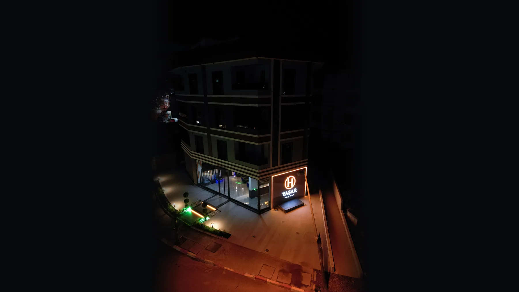 Ofisin bulunduğu bina, gece drone görünümü. Giriş üstündeki H YAŞAR İNŞAAT tabelası ve cephe aydınlatması yanıyor